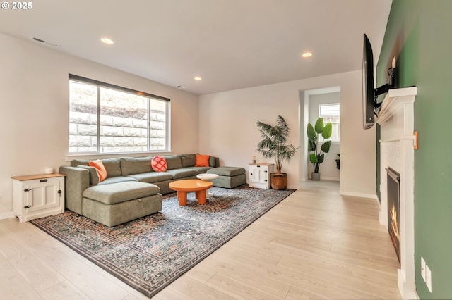 living area with a lit fireplace, light wood-type flooring, visible vents, and recessed lighting