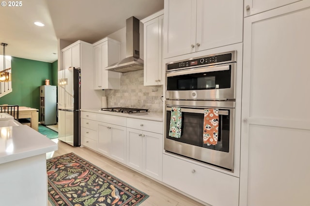 kitchen featuring tasteful backsplash, light countertops, appliances with stainless steel finishes, white cabinets, and wall chimney range hood