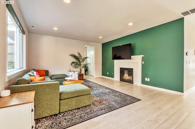 living area featuring baseboards, a fireplace, visible vents, and wood finished floors