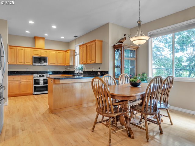 kitchen with appliances with stainless steel finishes, dark countertops, a peninsula, light brown cabinets, and pendant lighting