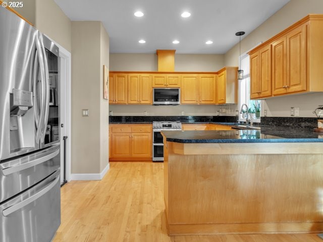 kitchen with appliances with stainless steel finishes, a peninsula, light wood-type flooring, pendant lighting, and a sink