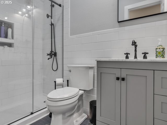 full bathroom featuring tile walls, toilet, a stall shower, vanity, and wainscoting