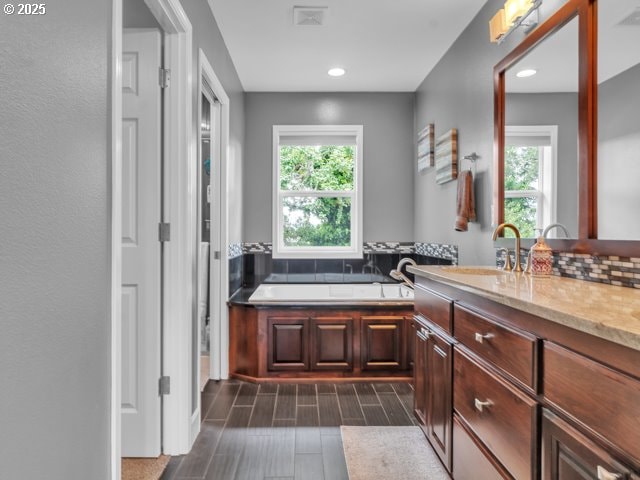 full bath featuring plenty of natural light, a garden tub, vanity, wood tiled floors, and recessed lighting