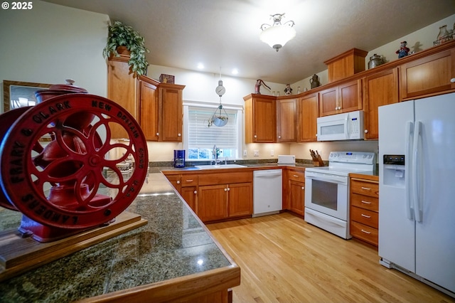 kitchen featuring white appliances, a sink, brown cabinetry, and light wood-style flooring
