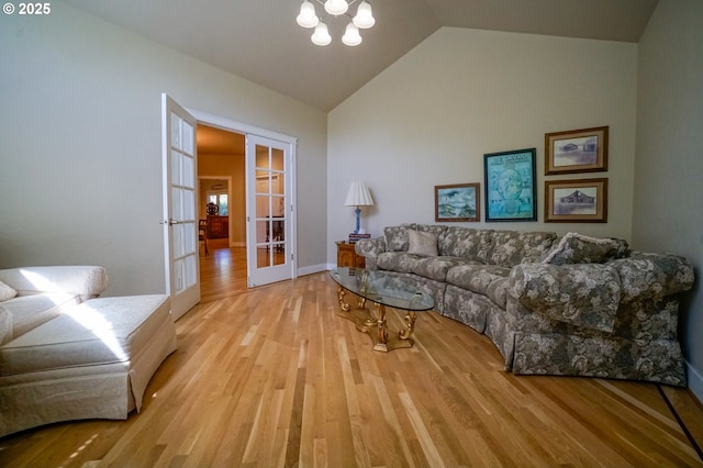 living room featuring french doors, light wood finished floors, lofted ceiling, a chandelier, and baseboards
