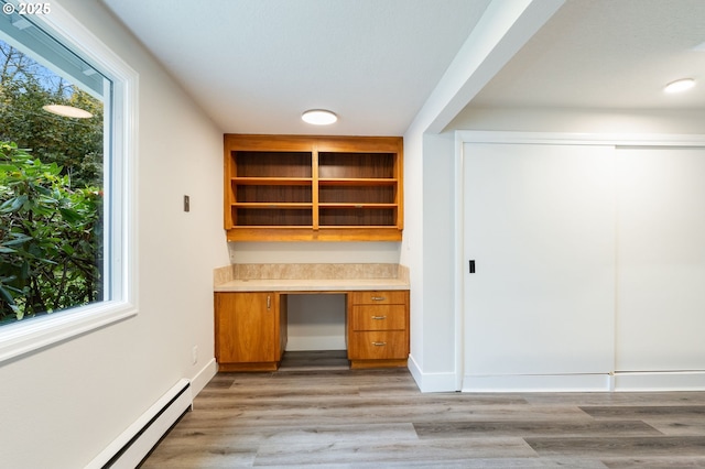 unfurnished office featuring a baseboard radiator, light hardwood / wood-style floors, a wealth of natural light, and built in desk