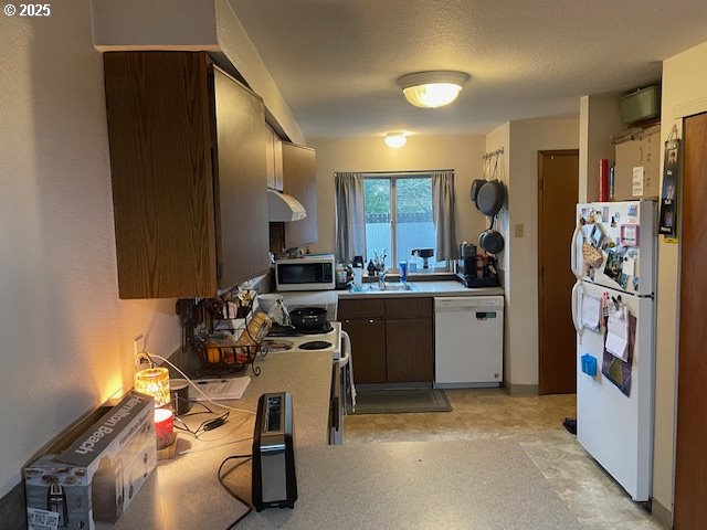 kitchen with light countertops, white appliances, a sink, and under cabinet range hood