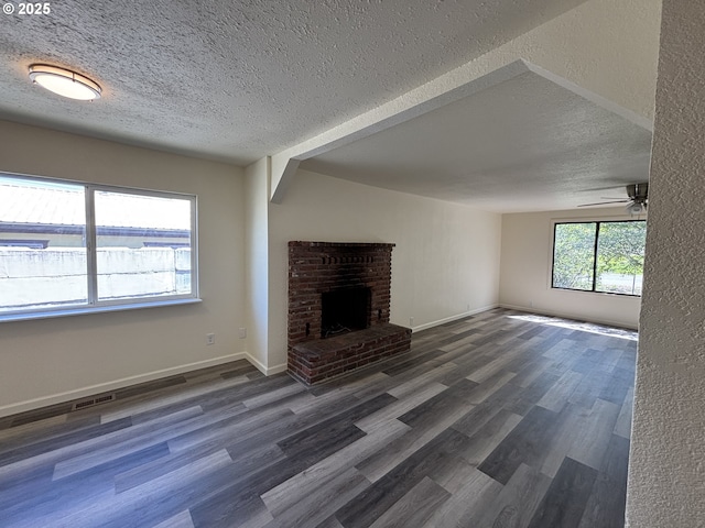 unfurnished living room with ceiling fan, a brick fireplace, a textured ceiling, baseboards, and wood finished floors