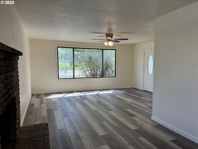 unfurnished living room featuring dark wood-style flooring, a fireplace, a textured ceiling, a ceiling fan, and baseboards