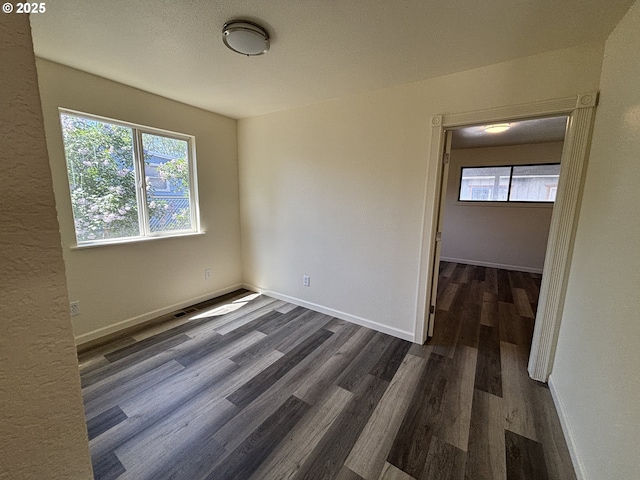 spare room with plenty of natural light, dark wood-style flooring, and baseboards