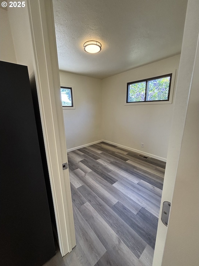 unfurnished room featuring plenty of natural light, a textured ceiling, dark wood finished floors, and visible vents