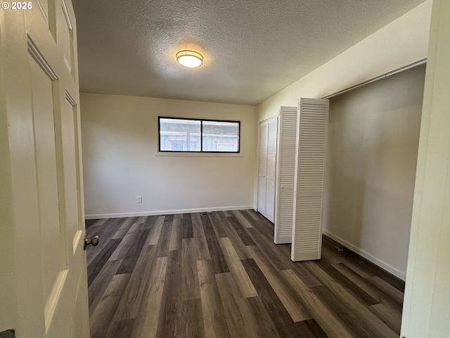unfurnished bedroom featuring baseboards, a textured ceiling, and dark wood-style flooring