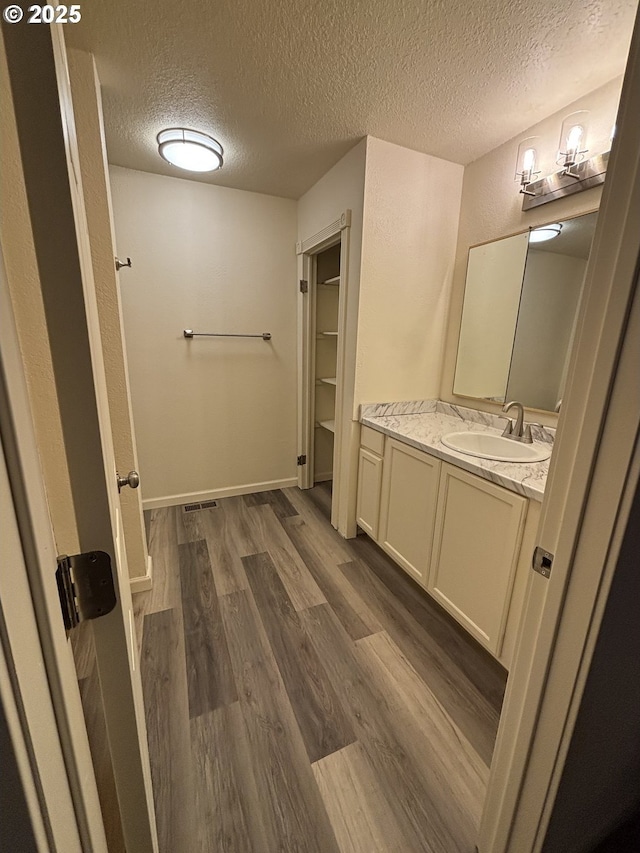 full bath with vanity, a textured ceiling, wood finished floors, a spacious closet, and visible vents