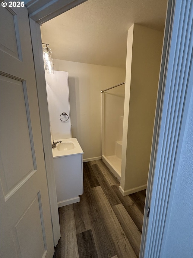 bathroom featuring baseboards, walk in shower, wood finished floors, and vanity