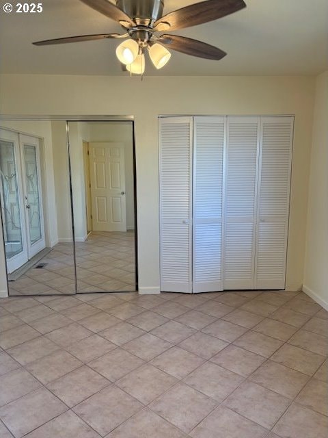 unfurnished bedroom with light tile patterned floors, baseboards, a ceiling fan, and two closets