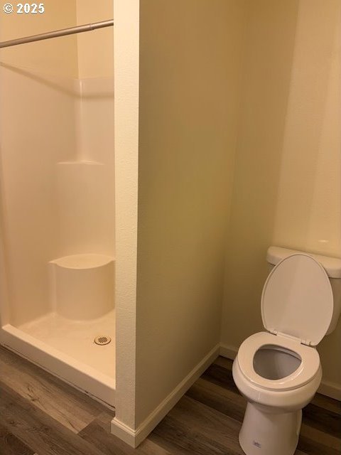 full bathroom with toilet, baseboards, wood finished floors, and a stall shower