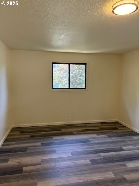 unfurnished room with baseboards, a textured ceiling, and dark wood-style flooring