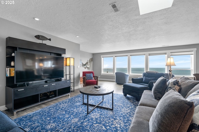 living room featuring visible vents, a textured ceiling, baseboards, and wood finished floors