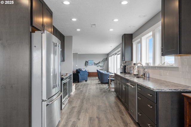 kitchen with stainless steel appliances, wood finished floors, a sink, visible vents, and tasteful backsplash