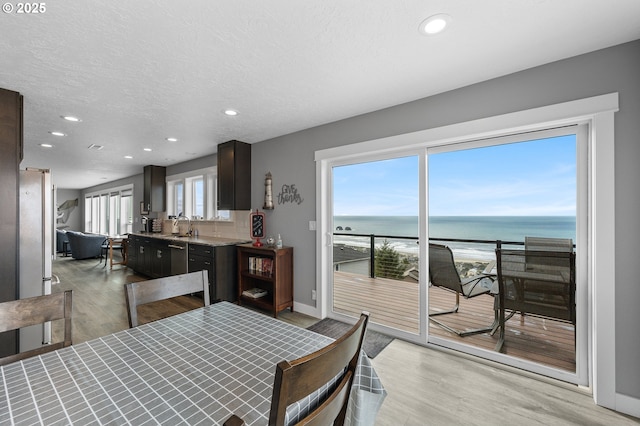 dining room featuring baseboards, light wood-style flooring, a water view, a textured ceiling, and recessed lighting