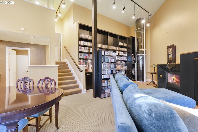 living room with rail lighting, light colored carpet, and a towering ceiling