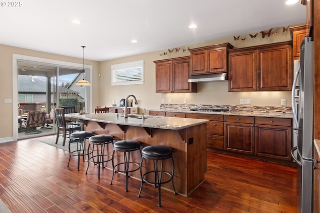 kitchen with dark wood-type flooring, stainless steel appliances, under cabinet range hood, and a sink