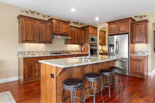 kitchen featuring dark wood-style floors, a breakfast bar, a sink, stainless steel appliances, and under cabinet range hood