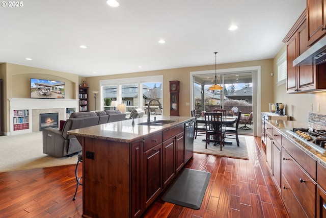 kitchen with dark wood finished floors, a breakfast bar area, appliances with stainless steel finishes, a fireplace, and a sink