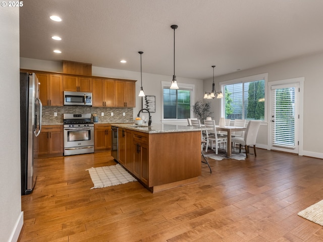 14420 SW Equestrian Ln, Beaverton, OR 97008 - kitchen with appliances with stainless steel finishes, a sink, light wood-style floors, brown cabinets, and tasteful backsplash