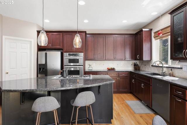 12453 SW Sheldrake Way, Beaverton, OR 97007 - kitchen with appliances with stainless steel finishes, a kitchen island, a sink, backsplash, and light wood finished floors