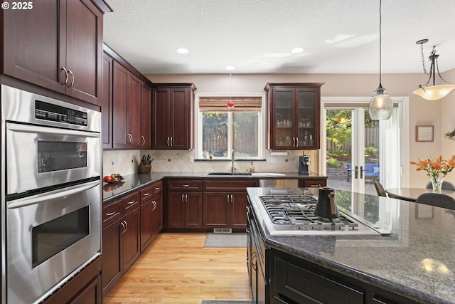 12453 SW Sheldrake Way, Beaverton, OR 97007 - kitchen featuring appliances with stainless steel finishes, a sink, backsplash, light wood-style floors, and dark stone countertops