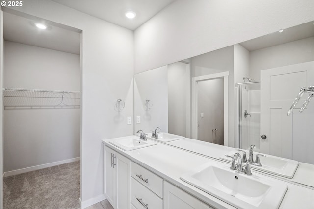 bathroom with a walk in closet, double vanity, a stall shower, and a sink