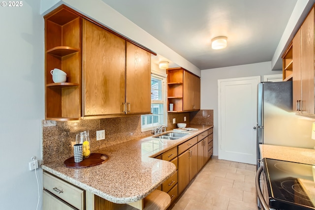 kitchen featuring open shelves, a sink, tasteful backsplash, brown cabinets, and light stone counters