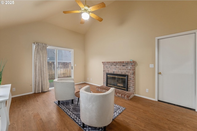 living area with wood finished floors, baseboards, lofted ceiling, ceiling fan, and a brick fireplace