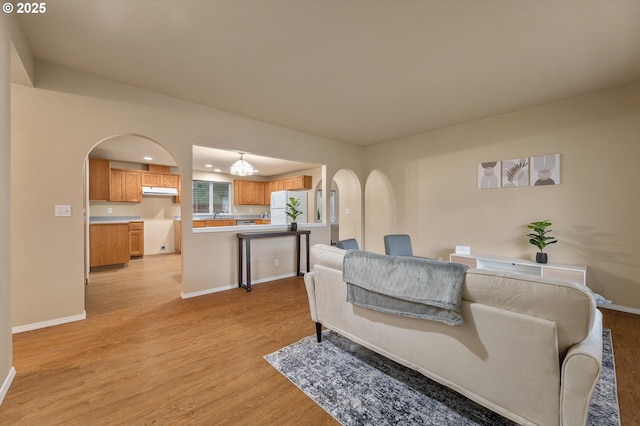 living room with baseboards, arched walkways, and light wood finished floors