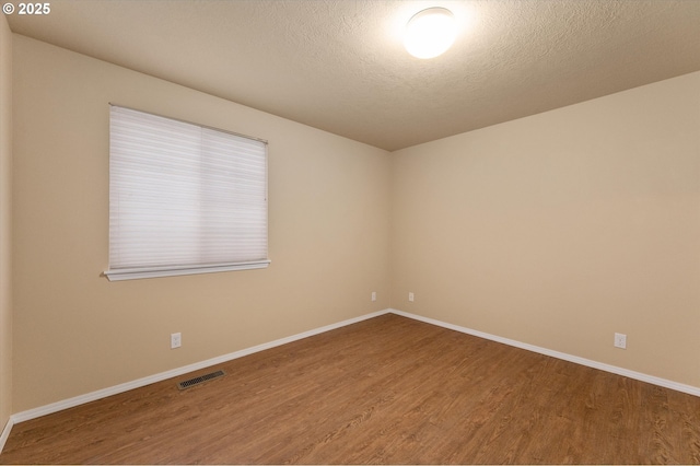 spare room with visible vents, baseboards, a textured ceiling, and wood finished floors