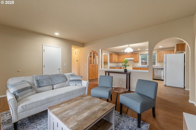 living room featuring arched walkways, recessed lighting, baseboards, and light wood-style floors