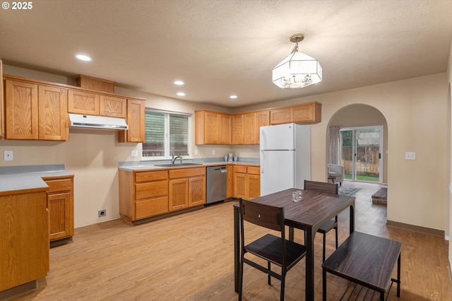 kitchen featuring a sink, stainless steel dishwasher, freestanding refrigerator, arched walkways, and light wood-style floors