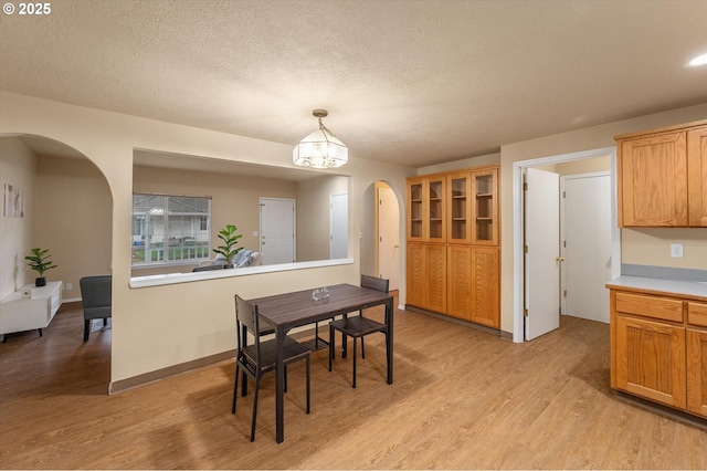 dining area featuring arched walkways, a textured ceiling, light wood-type flooring, and baseboards