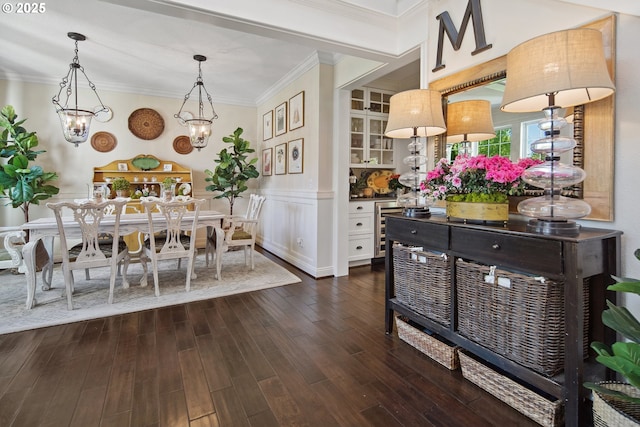 dining room featuring a notable chandelier, dark wood-style flooring, ornamental molding, and wainscoting