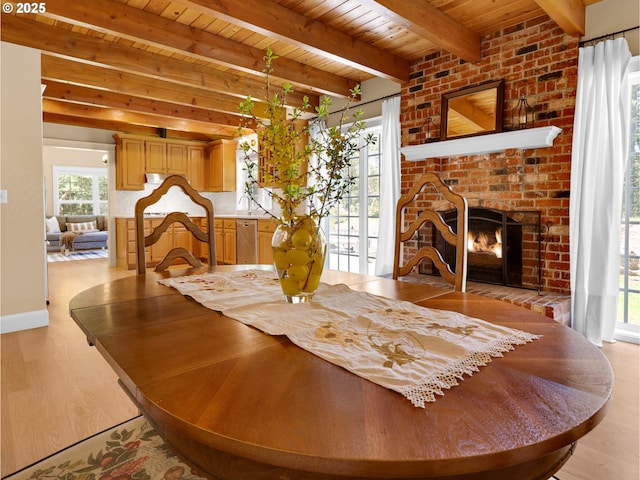 dining space featuring light wood-style floors, a brick fireplace, beam ceiling, and wooden ceiling