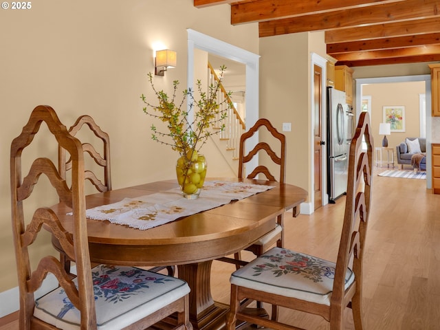 dining space with stairs, light wood finished floors, and beam ceiling