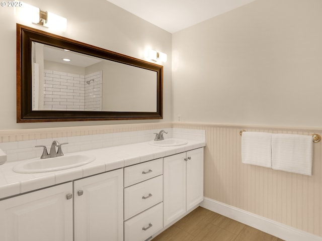 full bathroom featuring double vanity, a sink, wainscoting, and baseboards
