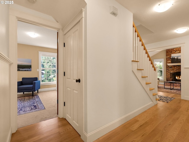 hallway with light wood-type flooring, stairs, and baseboards