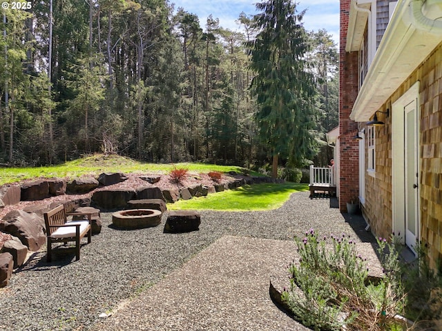 view of yard with a view of trees, an outdoor fire pit, and a deck