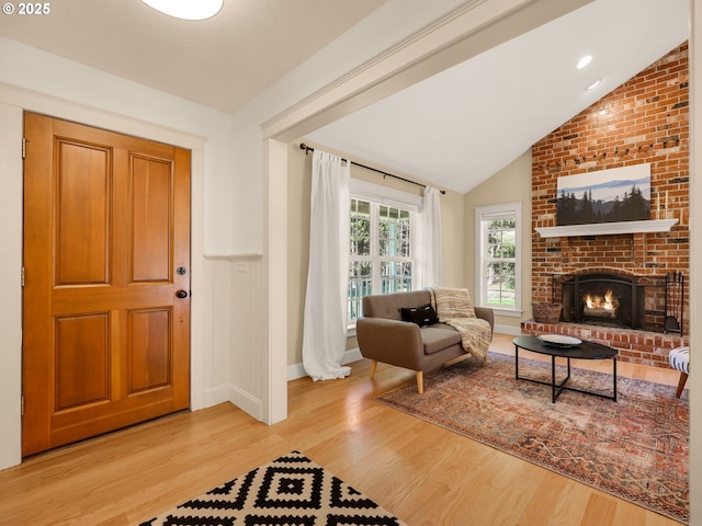 living room with baseboards, vaulted ceiling, light wood finished floors, and a brick fireplace