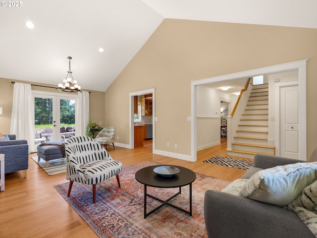 living area with a notable chandelier, light wood-style floors, high vaulted ceiling, stairs, and baseboards