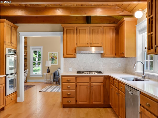 kitchen with a healthy amount of sunlight, a sink, beamed ceiling, under cabinet range hood, and stainless steel appliances