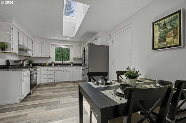 5323 Verda Ln, Keizer, OR 97303 - kitchen with stainless steel appliances, a skylight, under cabinet range hood, white cabinetry, and light wood-style flooring
