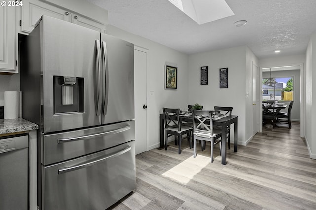 5323 Verda Ln, Keizer, OR 97303 - kitchen featuring stainless steel refrigerator with ice dispenser, a skylight, white dishwasher, light wood-style floors, and a textured ceiling